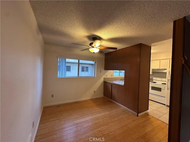 interior space featuring a ceiling fan, light wood-style floors, a wealth of natural light, baseboards, and a textured ceiling