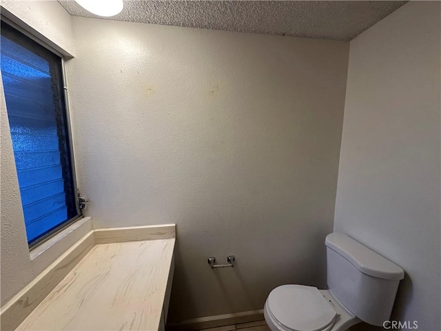 bathroom with a textured ceiling, toilet, and baseboards
