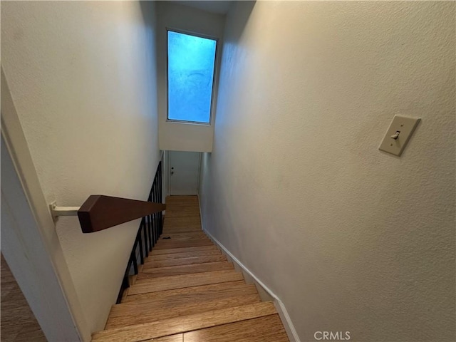 stairway featuring wood finished floors, baseboards, and a textured wall