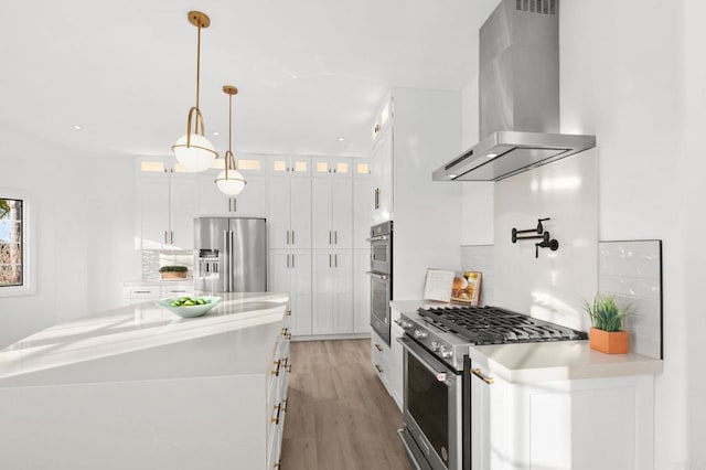 kitchen featuring wall chimney range hood, white cabinets, stainless steel appliances, and glass insert cabinets