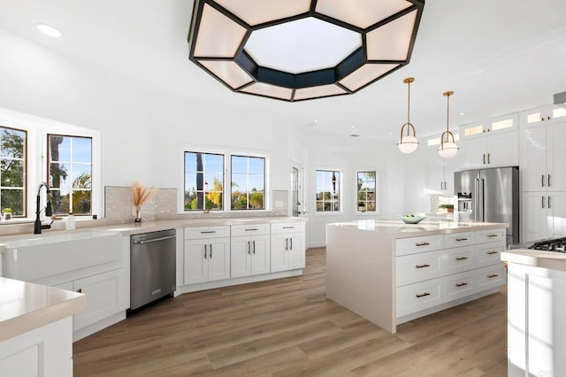 kitchen featuring light countertops, light wood-style flooring, tasteful backsplash, appliances with stainless steel finishes, and a sink