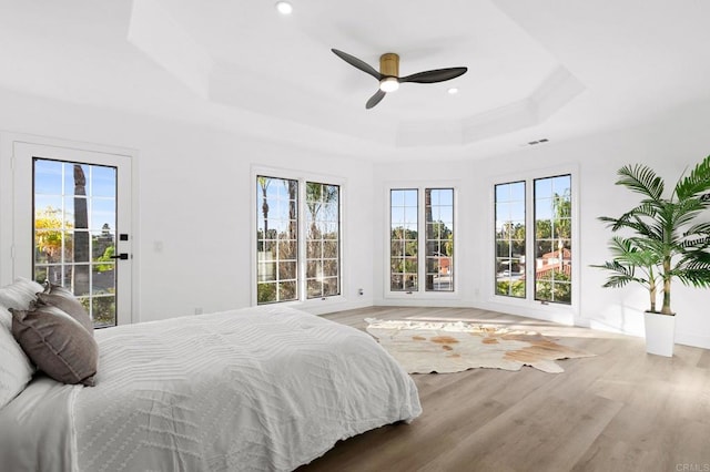 bedroom with a tray ceiling, access to exterior, wood finished floors, baseboards, and visible vents