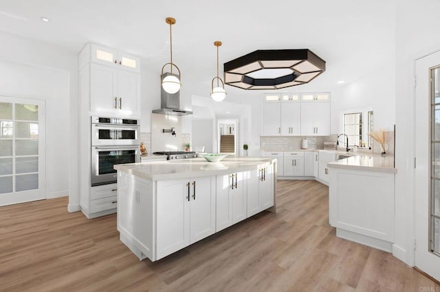 kitchen featuring light countertops, stainless steel appliances, a sink, light wood finished floors, and glass insert cabinets