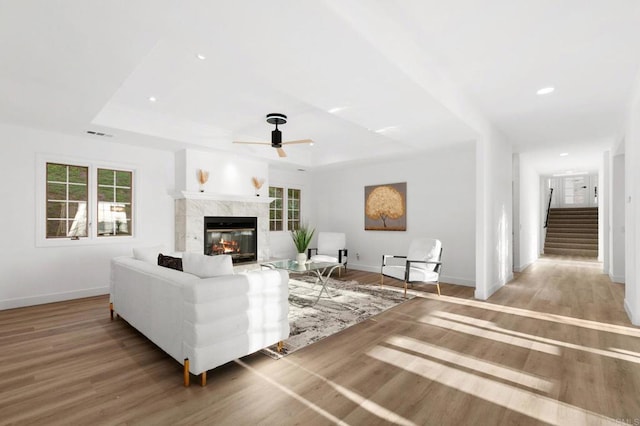 living room with a ceiling fan, stairway, light wood-type flooring, and a raised ceiling