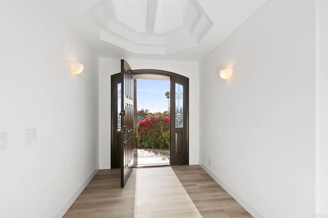 foyer featuring arched walkways, baseboards, and light wood-type flooring