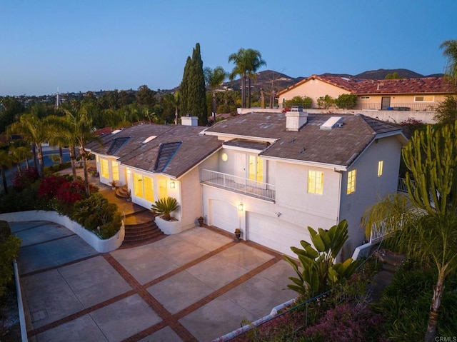 view of front facade featuring concrete driveway, stucco siding, an attached garage, a balcony, and a chimney
