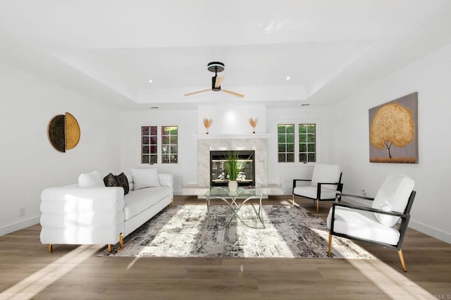 living room featuring baseboards, a tray ceiling, wood finished floors, and ceiling fan