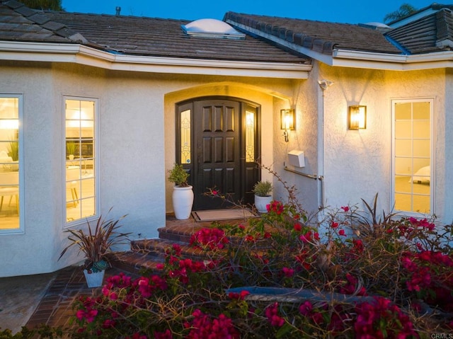 view of exterior entry with stucco siding and a tile roof