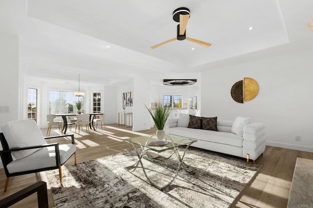 living area featuring baseboards, ceiling fan, wood finished floors, and a raised ceiling