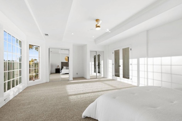 carpeted bedroom featuring visible vents, two closets, baseboards, a raised ceiling, and french doors