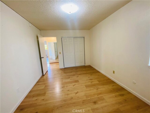 unfurnished bedroom featuring a closet, light wood-style flooring, a textured ceiling, and baseboards