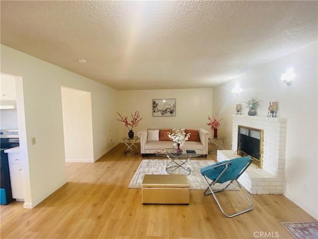 living room featuring light wood-style flooring, a fireplace, a textured ceiling, and baseboards