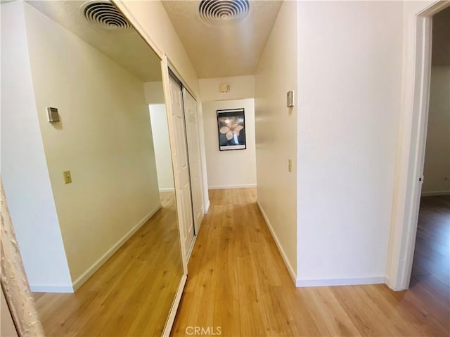 hallway featuring light wood-style floors, visible vents, and baseboards