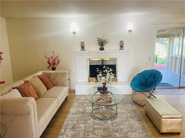 living area with a brick fireplace, a textured ceiling, and wood finished floors