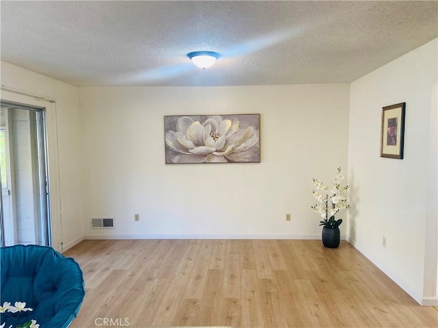 unfurnished room with baseboards, visible vents, light wood finished floors, and a textured ceiling