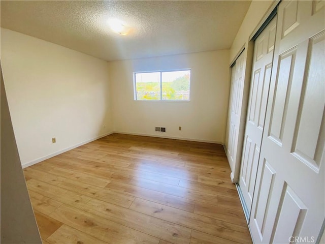 unfurnished bedroom with visible vents, baseboards, multiple closets, light wood-type flooring, and a textured ceiling