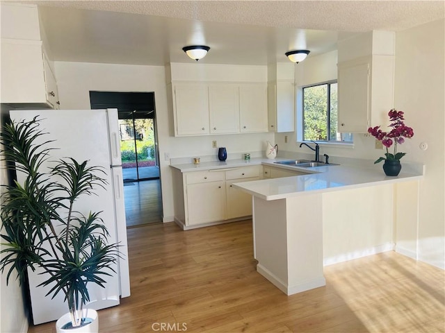 kitchen featuring light wood finished floors, a peninsula, freestanding refrigerator, a sink, and light countertops
