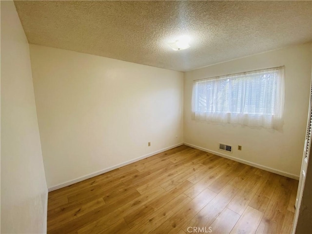 empty room with visible vents, baseboards, a textured ceiling, and light wood finished floors