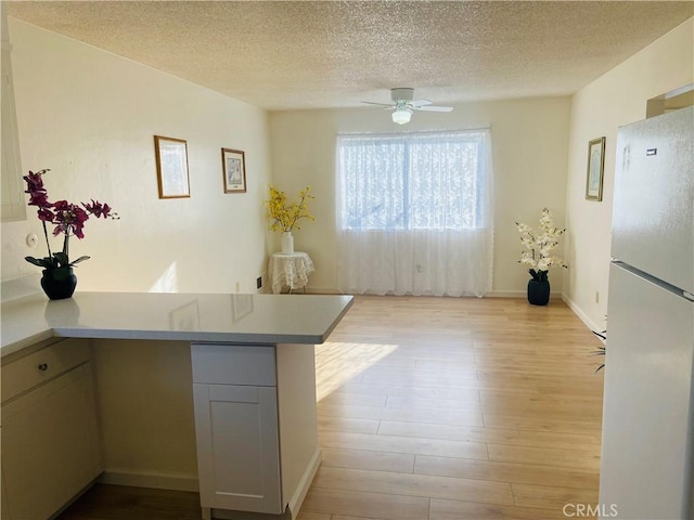 kitchen featuring a ceiling fan, a textured ceiling, freestanding refrigerator, a peninsula, and light wood finished floors