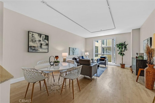dining space with light wood finished floors, baseboards, and attic access