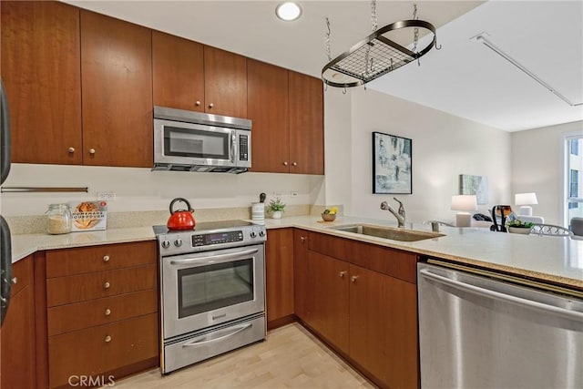 kitchen with stainless steel appliances, a sink, light wood finished floors, open floor plan, and a peninsula