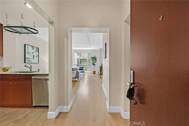 hallway featuring a sink, light wood finished floors, and baseboards