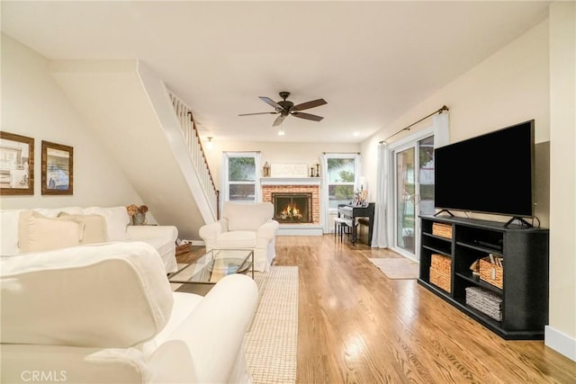 living area featuring a brick fireplace, light wood finished floors, and ceiling fan