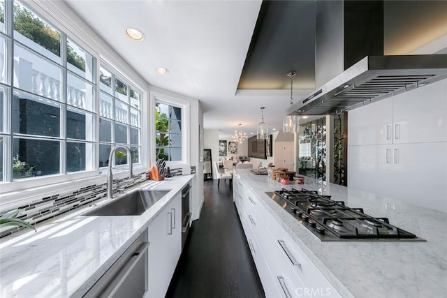 kitchen featuring wall chimney range hood, white cabinets, appliances with stainless steel finishes, a sink, and a notable chandelier