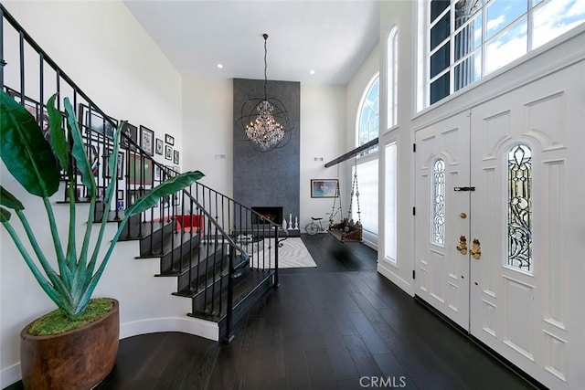 entrance foyer with a notable chandelier, a towering ceiling, baseboards, stairs, and wood-type flooring