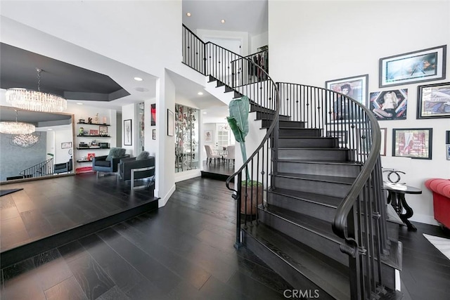 staircase featuring baseboards, an inviting chandelier, wood finished floors, and a high ceiling