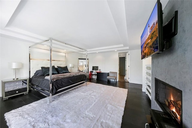 bedroom featuring baseboards, a warm lit fireplace, recessed lighting, a tray ceiling, and wood finished floors
