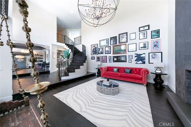 living area featuring baseboards, a notable chandelier, stairway, wood finished floors, and a towering ceiling