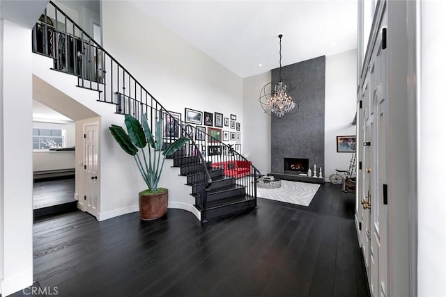 entryway with a large fireplace, a chandelier, dark wood-style floors, a high ceiling, and stairs
