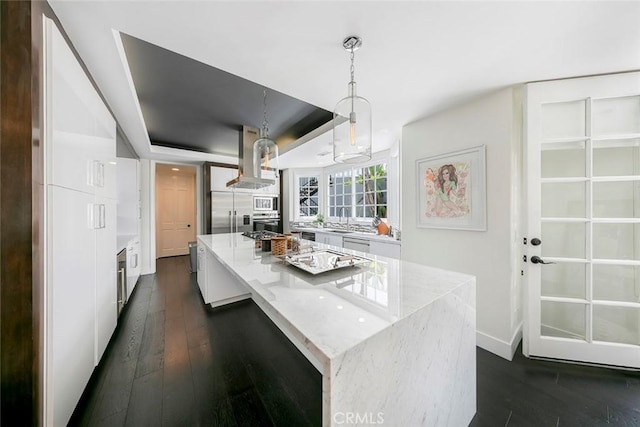 kitchen with dark wood-type flooring, white cabinets, island exhaust hood, a raised ceiling, and built in appliances