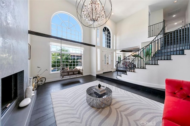 interior space with a towering ceiling, a fireplace with raised hearth, wood finished floors, stairs, and baseboards