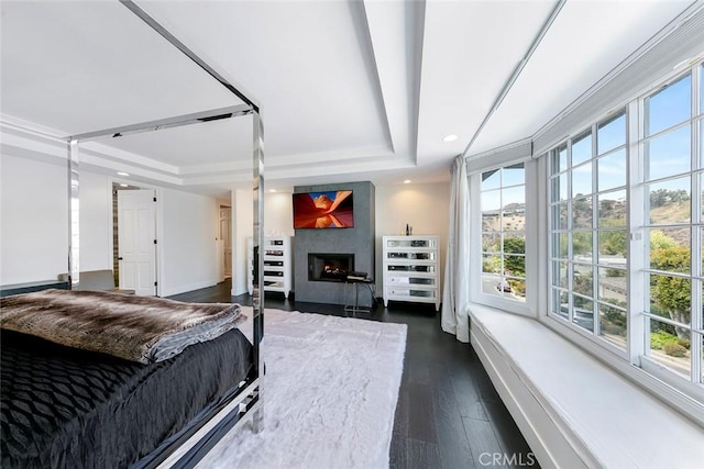 bedroom featuring dark wood finished floors, a warm lit fireplace, recessed lighting, a raised ceiling, and baseboards