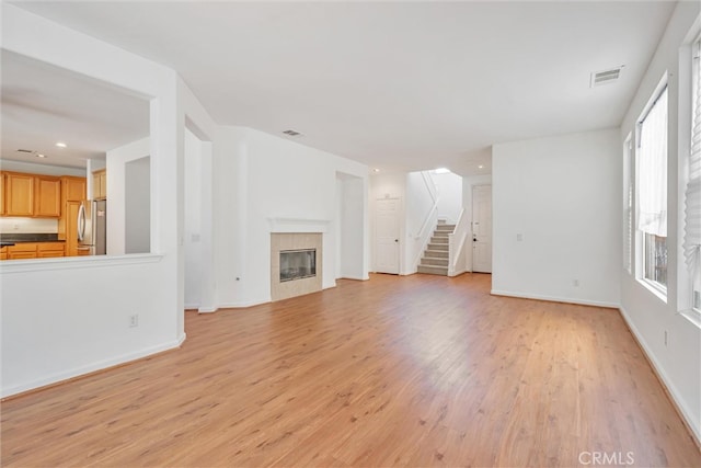 unfurnished living room with stairway, light wood-style flooring, visible vents, and a tile fireplace