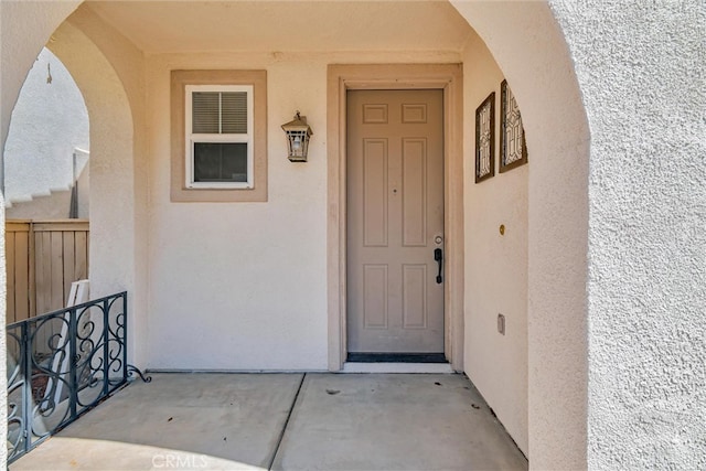 property entrance with stucco siding and fence
