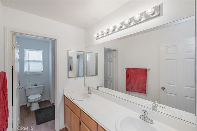 bathroom featuring double vanity, wood finished floors, toilet, and a sink