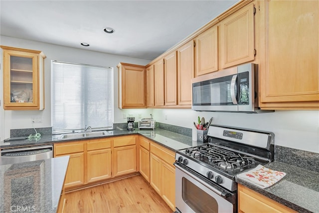 kitchen with dark stone countertops, a sink, light brown cabinetry, stainless steel appliances, and light wood-type flooring