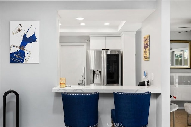 kitchen with a peninsula, stainless steel fridge with ice dispenser, tile patterned floors, and white cabinets