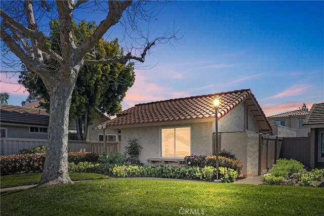 view of property exterior featuring fence, a tiled roof, a yard, and stucco siding