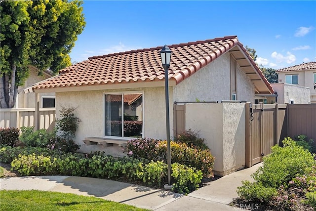 view of side of home featuring fence, a tile roof, and stucco siding