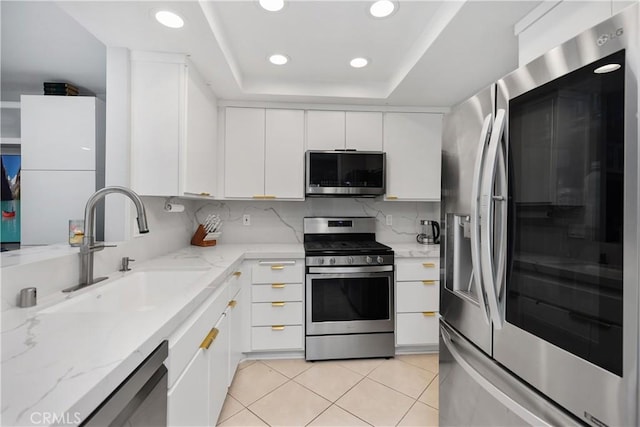 kitchen with a sink, a tray ceiling, white cabinets, appliances with stainless steel finishes, and recessed lighting