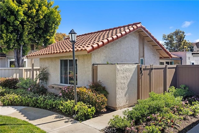 view of side of home featuring stucco siding, a tiled roof, and fence