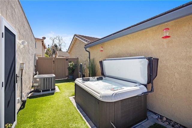 view of yard with central AC, a gate, fence, and a hot tub