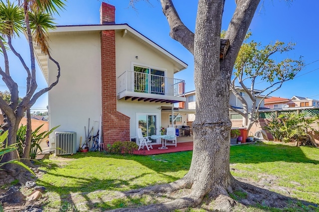 rear view of house featuring a balcony, stucco siding, central AC, and a lawn