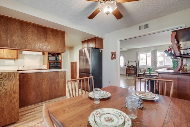 dining area with light wood-style flooring, visible vents, a ceiling fan, and a textured ceiling