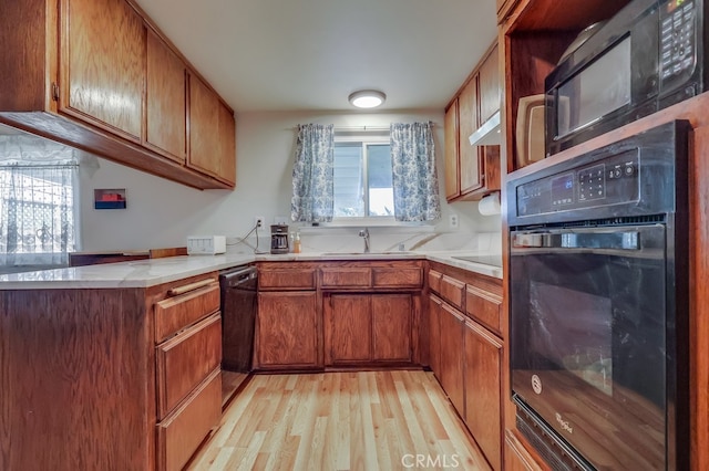 kitchen featuring light countertops, light wood-type flooring, a sink, and black appliances