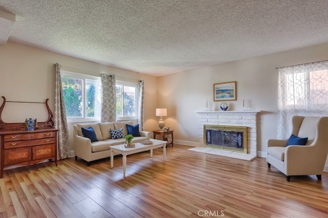living area featuring baseboards, a fireplace, light wood-type flooring, and a textured ceiling
